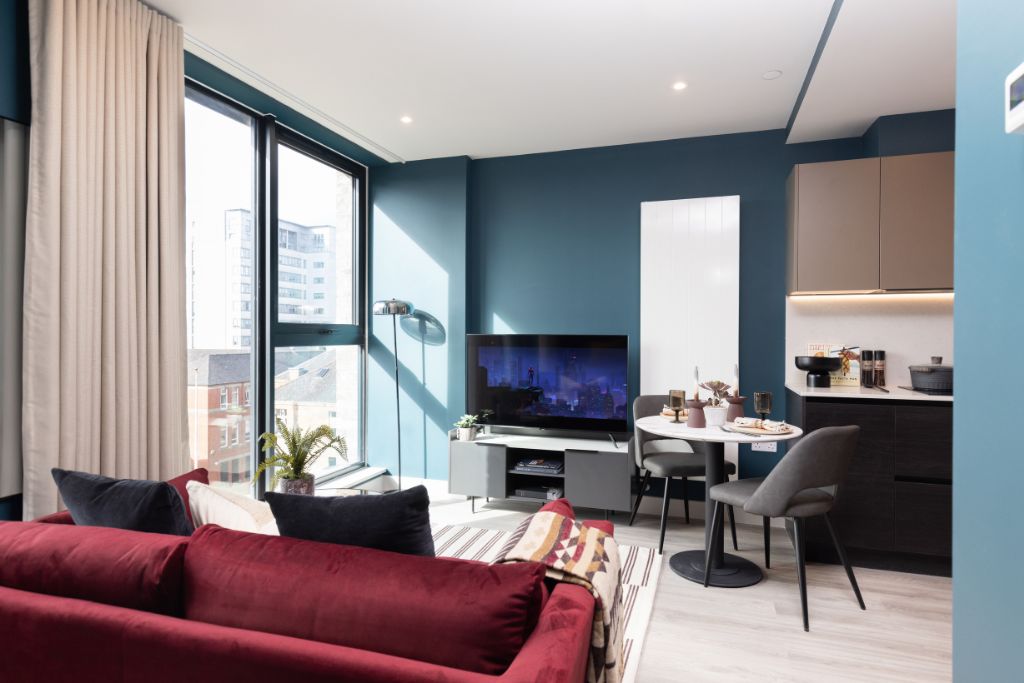 Studio apartment interior at 50 Holland Street, featuring modern furnishings, large windows, a red sofa, dining table, and kitchenette, highlighting pet-friendly living and contemporary design in Glasgow’s cultural quarter.