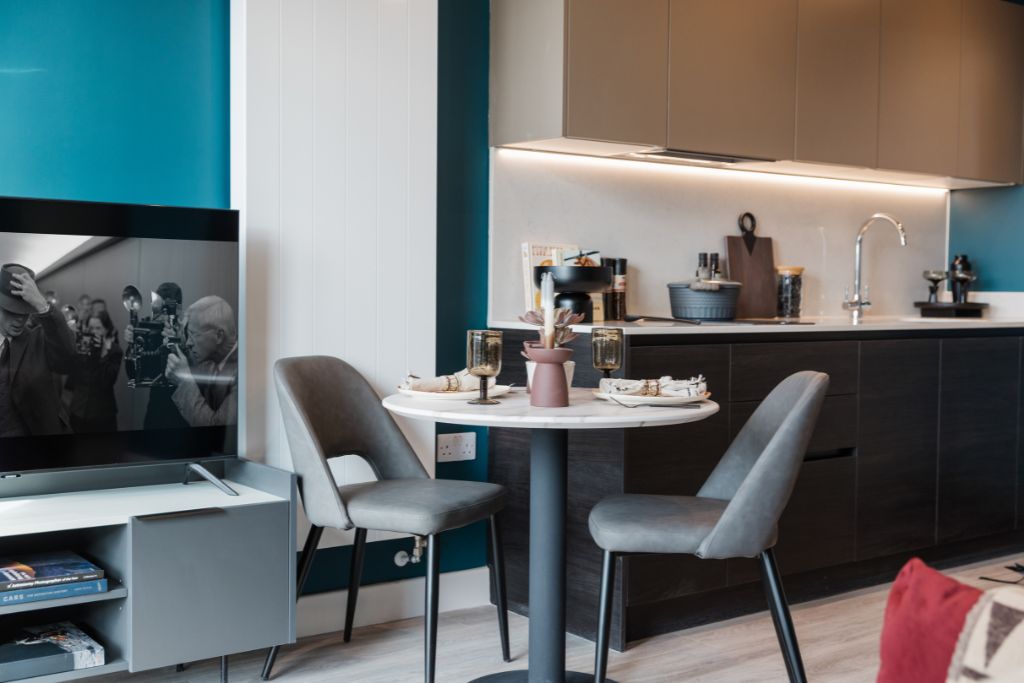 Studio apartment interior with modern kitchen, dining table, and television displaying black-and-white image, showcasing stylish furnishings and contemporary decor in Glasgow’s cultural quarter.