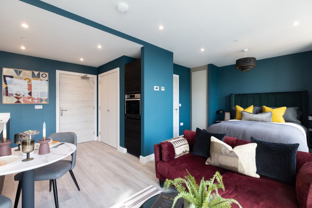 Studio apartment interior at 50 Holland Street, featuring modern furnishings, a dining area, a cozy sofa, and a stylish bedroom with teal walls and decorative accents, highlighting pet-friendly living and contemporary design.