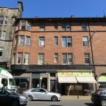 Two-bedroom flat on Great Junction Street, Edinburgh, featuring a red brick exterior, nearby vehicles, and local businesses, highlighting the property's location for rent at &pound;1,295 pcm.