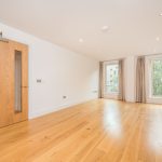 Spacious and bright living area in unfurnished one-bedroom flat at 6/3 Brandfield Street, Edinburgh, featuring wooden flooring, large windows with curtains, and modern door leading to outdoor space.