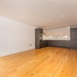 Spacious unfurnished flat interior featuring wooden flooring, modern kitchen units, and ample natural light, located at 6/3 Brandfield Street, Edinburgh.