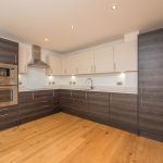 Modern kitchen with dark wood cabinets, integrated appliances, and wooden flooring in a one-bedroom unfurnished flat for rent at 6/3 Brandfield Street, Edinburgh.