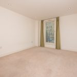 Spacious unfurnished living room in a one-bedroom flat at 6/3 Brandfield Street, Edinburgh, featuring large window with green curtains and neutral decor.
