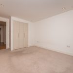 Spacious unfurnished bedroom with built-in wardrobes in a one-bedroom flat at 6/3 Brandfield Street, Edinburgh, featuring neutral decor and carpeted flooring.