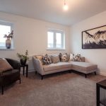 Living room of a 4-bedroom unfurnished terraced house in South Queensferry, featuring a corner sofa, decorative cushions, a coffee table, and large windows with natural light.