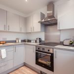 Modern kitchen in unfurnished 4-bedroom terraced house for rent in South Queensferry, featuring grey cabinets, integrated appliances, and wooden flooring.