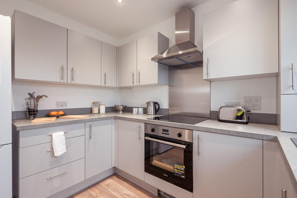 Modern kitchen in a 4-bedroom unfurnished terraced house, featuring grey cabinetry, stainless steel appliances, and a countertop with utensils and fruit, located in South Queensferry.