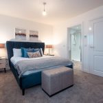 Bedroom in unfurnished 4-bedroom terraced house, featuring a double bed with blue upholstered headboard, decorative cushions, bedside lamps, and en suite bathroom access.