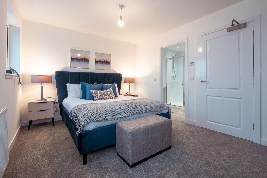 Modern bedroom featuring a plush blue bed, stylish decor, bedside lamps, and an en suite bathroom, showcasing unfurnished accommodation in a 4-bedroom terraced house for rent in South Queensferry.