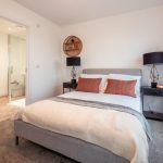 Modern bedroom in unfurnished 4-bedroom terraced house, featuring a double bed with decorative cushions, bedside tables with lamps, and an en suite bathroom visible in the background, located in South Queensferry.