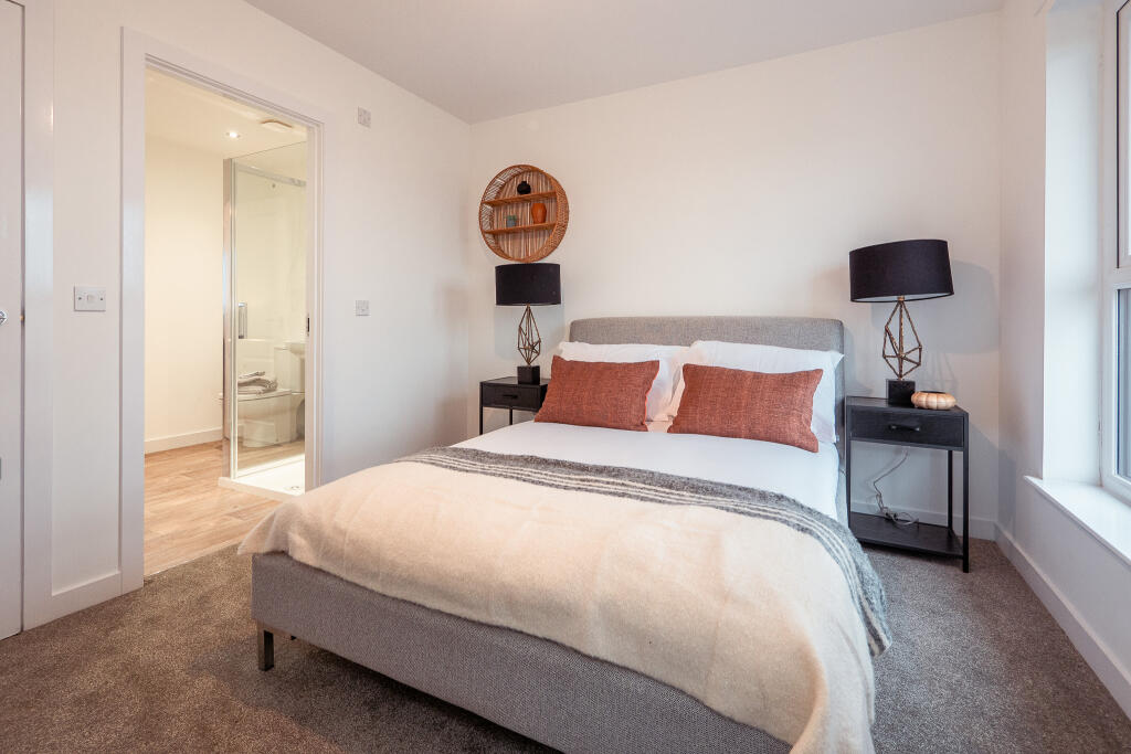 Bedroom in a 4-bedroom terraced house in South Queensferry, featuring a double bed with decorative pillows, bedside tables with lamps, and an en suite bathroom visible through an open door.