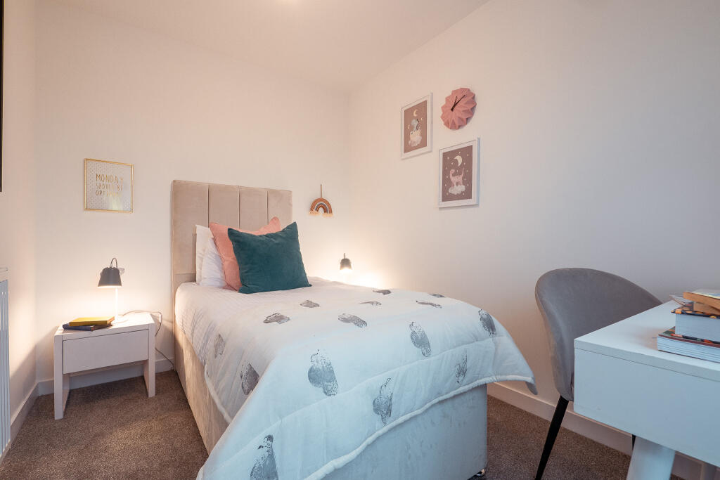 Cozy bedroom in unfurnished 4-bedroom terraced house, featuring a bed with decorative pillows, bedside lamp, desk, and wall art in South Queensferry.