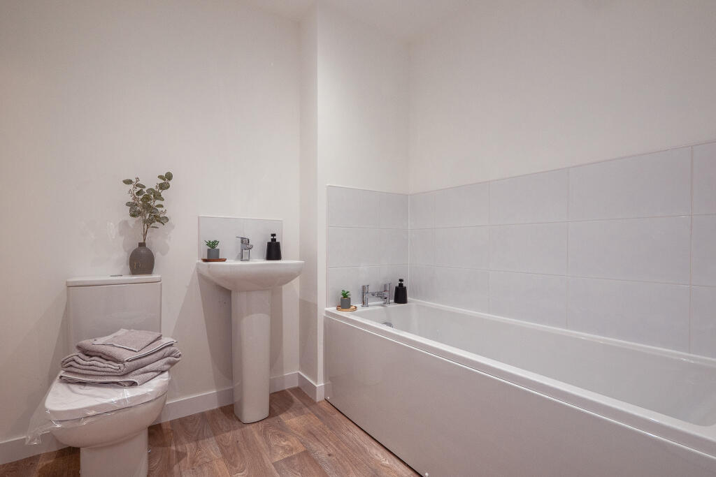 Modern bathroom featuring a white bathtub, sink, and toilet, with decorative plants and neatly stacked towels, emphasizing the unfurnished 4-bedroom terraced house in South Queensferry.