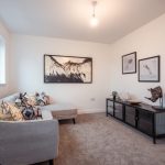 Living room of an unfurnished 4-bedroom terraced house in South Queensferry, featuring a grey sofa, decorative cushions, wall art, and a stylish storage unit.