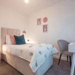 Bedroom in unfurnished 4-bedroom terraced house, featuring single bed with decorative cushions, chair, and wall art in light, modern decor.