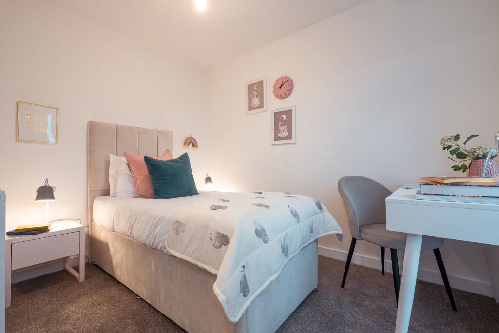 Unfurnished bedroom in 4-bedroom terraced house, featuring a bed with decorative pillows, bedside table with lamp, desk with chair, and wall art, located in South Queensferry.