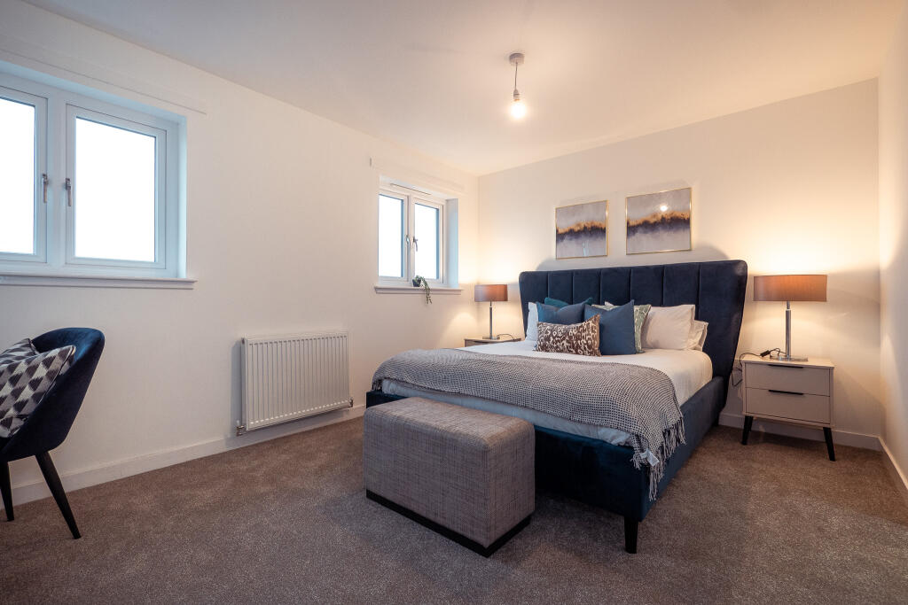 Spacious, unfurnished bedroom in a 4-bedroom terraced house, featuring a large bed with decorative pillows, bedside tables with lamps, a stylish chair, and modern artwork, located in South Queensferry.