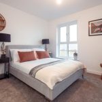 Modern bedroom with double bed, decorative pillows, bedside tables, and windows, showcasing unfurnished accommodation in a 4-bedroom terraced house in South Queensferry.