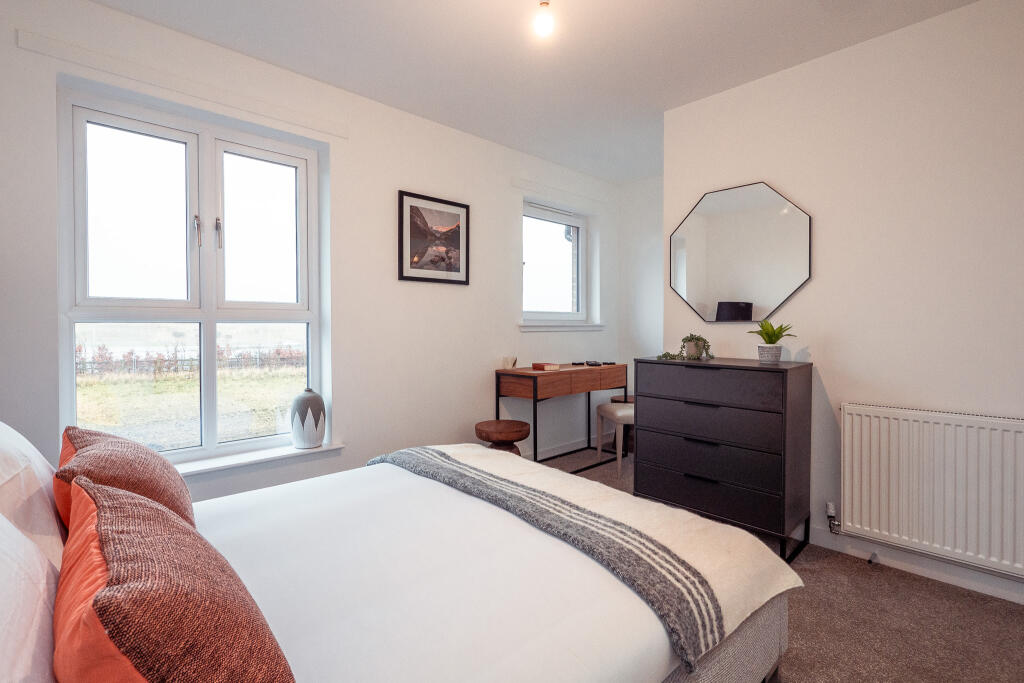Bright and modern bedroom featuring a double bed with decorative cushions, a stylish dresser, a desk with a chair, and large windows providing natural light, suitable for a 4-bedroom terraced house in South Queensferry available to let.