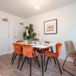 Dining area featuring a round table with orange chairs, decorative plant, and framed artwork in an unfurnished 4-bedroom terraced house in South Queensferry.