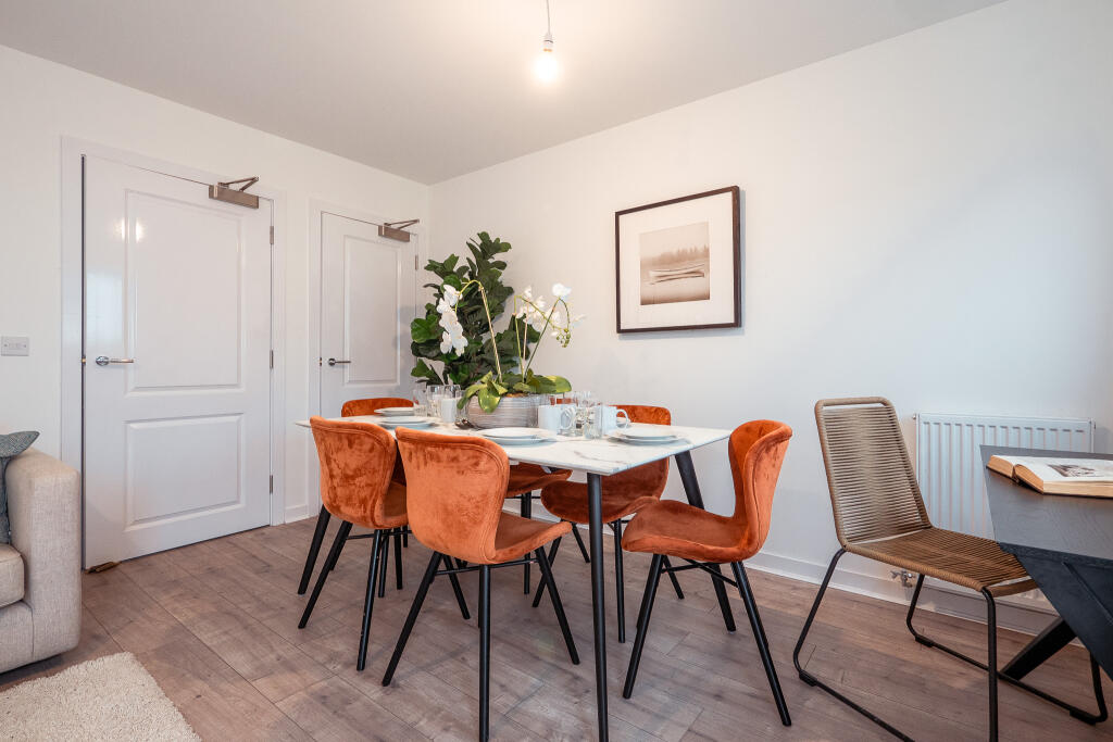 Dining area in a terraced house featuring a round table set for meals, surrounded by orange velvet chairs, with a potted plant and artwork on the wall, highlighting the unfurnished accommodation in South Queensferry.